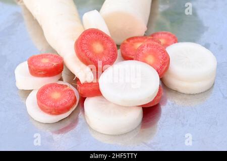 Nahaufnahme des Bündels in Scheiben geschnittene rote Karotte mit weißem Rettich über unscharf grauem Hintergrund. Stockfoto