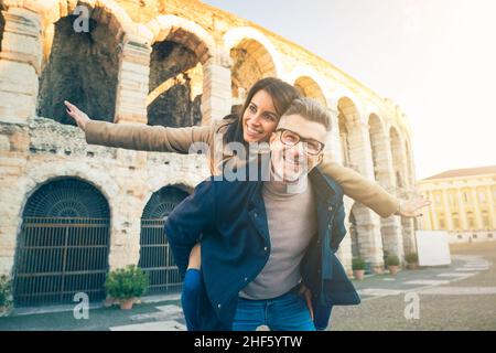 Glückliches Senior-Paar in der Liebe Spaß vor dem berühmten Denkmal von Italien. Fröhliche Frau streckt die Arme aus, während sie auf dem Rücken sitzt Stockfoto