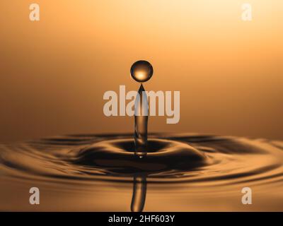 Makrofoto von Wassertropfen, die in einen Wasserlache fallen und einen Spritzer verursachen. Hochgeschwindigkeitsfotografie mit Blitzlicht, die zum Einfrieren der Action verwendet wird. Golden BA Stockfoto