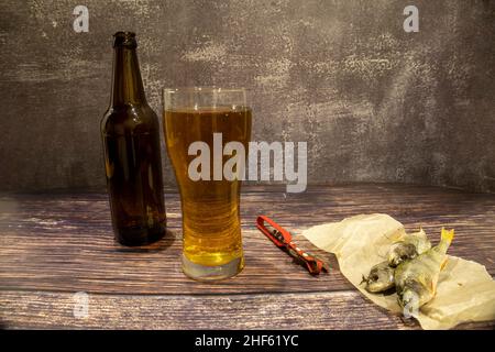 Bier mit getrocknetem Fisch und Öffner auf Holzboden Stockfoto