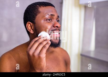 afroamerikanischer Mann, der sich im Badezimmerspiegel ansah und dabei den Noppen drückte Stockfoto