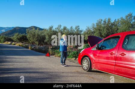 Ein Mann mit entspannter Haltung strandete auf der Straße neben dem kaputten Auto und sprach am Telefon Stockfoto