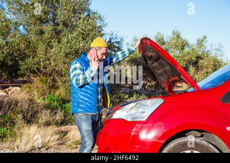 Bärtiger Mann, der auf der Straße neben seinem heruntergekommenen Auto telefonierte Stockfoto
