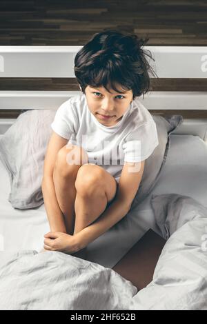 Kleiner Junge, der an Schlafstörungen leidet, sitzt in seinem Bett Stockfoto