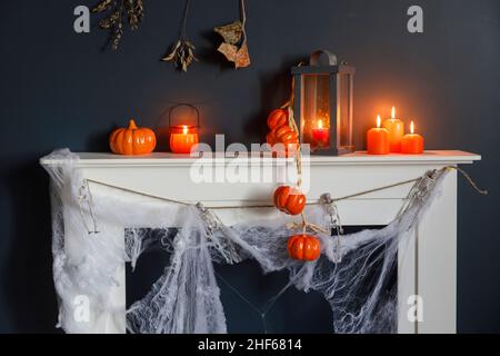 Halloween-Heimtextilien. Plastikspielzeug-Skelette in einer Holzkiste am Kamin vor einer dunkelblauen Wand. Eine Girlande aus Skeletten. Spinnennetz auf den dres Stockfoto