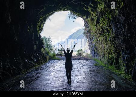 Silhouette einer nicht erkennbaren Frau, die aus einem dramatischen Tunnel in der alten Sao Vicente Straße in den Bergen der Insel Madeira herausschaut. Stockfoto