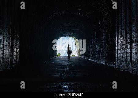 Silhouette einer nicht erkennbaren Frau, die aus einem dramatischen Tunnel in der alten Sao Vicente Straße in den Bergen der Insel Madeira herausschaut. Stockfoto