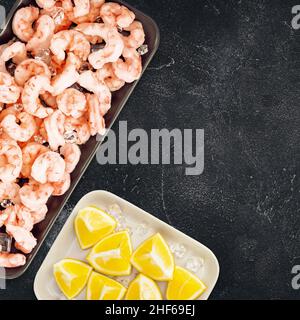 Lebensmittelbanner mit gefrorenen, gefüllten Garnelen mit Eiswürfeln und Zitronenscheiben auf einem schwarzen Steinhintergrund mit Platz zum Kopieren. Mittelmeer, Keto-Diät. Garnelen c Stockfoto