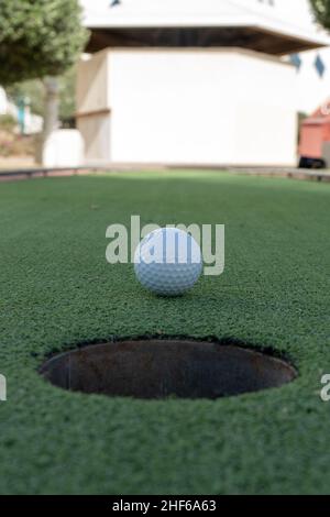 Miniatur- oder Minigolf-Loch in Nahaufnahme mit Ball in der Mitte auf grünem Kunstrasen im Freien (Porträtansicht) Stockfoto