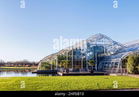 Blick auf die Vorderseite des berühmten Glasshouse und den See im RHS Garden, Wisley, Surrey an einem sonnigen Tag im Winter an einem sonnigen Tag mit blauem Himmel Stockfoto