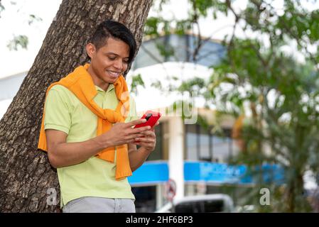 Hübscher junger Latino-Mann, der sein Mobiltelefon auf der Straße benutzt. Stockfoto
