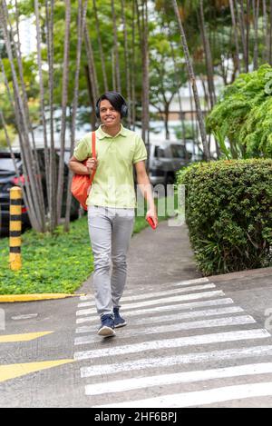 Ein junger Latino-Mann, der mit dem Telefon in der Hand die Straße entlang läuft Stockfoto
