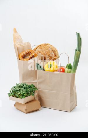 Papiertüten gefüllt mit goldenem Gebäck und buntem Gemüse daneben befindet sich ein Gartenbett auf weißem Hintergrund. Umweltfreundliche kompostierbare Taschen. Stockfoto