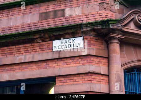 Zurück Piccadilly Straßenschild auf einem weißen Schild in schwarzer Schrift auf einer roten Backsteinmauer im Stadtzentrum von Manchester, Großbritannien. In der Nähe des zentralen Piccadilly Trai Stockfoto