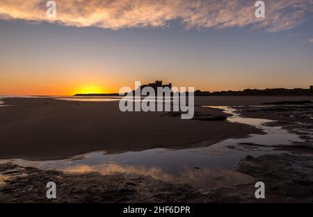 Das ikonische Bamburgh Castle bei Sonnenaufgang, mit dem Marrammgras auf den Dünen im Vordergrund Stockfoto