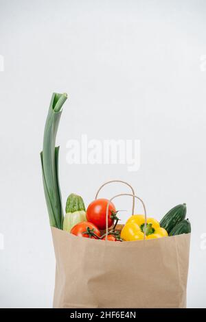 Lebensmittelpapierbeutel gefüllt mit buntem Gemüse auf weißem Hintergrund. Stockfoto