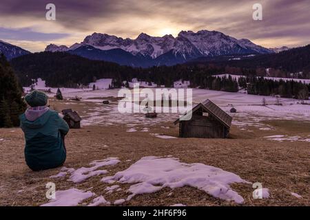 Frau sitzt bei Sonnenaufgang am Geroldsee bei Mittenwald / Krün und blickt in die Ferne, im Hintergrund das Karwendelgebirge, Bayern, Deutschland Stockfoto