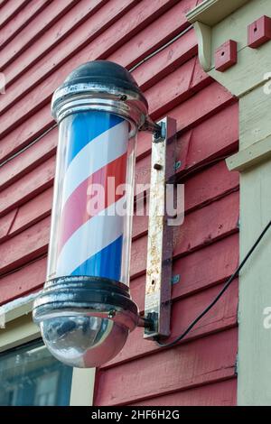 Barbershop-Stange mit roten, blauen und weißen Streifen, die sich außen an einem Friseurladen bewegen. Der nostalgische Vintage-Stock ist an einer Wand befestigt. Stockfoto