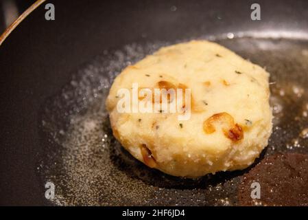 Eine einzelne ungekochte runde, zum Braten zubereitete Kabeljaufischekuchen mit Salz. Die Mischung aus Bohnenkraut, Kartoffel, Salz-Kabeljau und Butter wird zu einem kleinen Patty geformt. Stockfoto