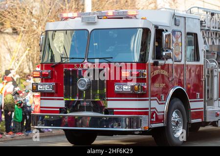 Ein großer rot-weißer Feuerwehrwagen von der St. John's Regional Fire Station fährt eine kleine Straße entlang mit Menschen auf der Beifahrerseite des Fahrzeugs Stockfoto