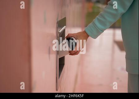 Eine Frau wirft eine Tasse Kaffee in einen Mülltonnen in der Wand eines Cafés. Stockfoto