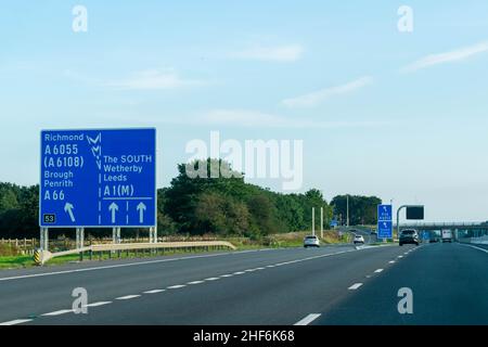 Leeds, Großbritannien - 23rd. August 2019: Autos fahren auf der britischen Autobahn A1 mit blauen Autobahnschildern, die die Fahrer nach Richmond, Leeds, Brough, Wetherby, Stockfoto
