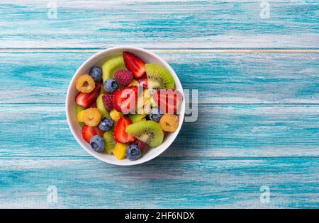 Natürliche Bio-Lebensmittel für ein gesundes und ernährungsförderliches Leben. Blick von oben auf frischen Obstsalat mit Kiwi, Erdbeere, Heidelbeere, Himbeere und Pfirsich auf blauem Holz Stockfoto