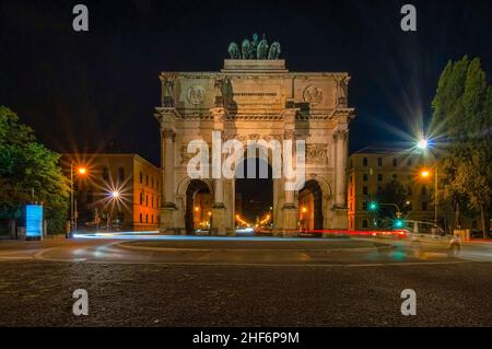 Siegestor in München bei Nacht mit einem Auto im Vordergrund. Stockfoto