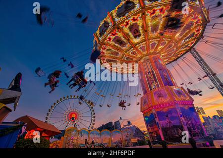 Kettenkarusel mit Silhoutten von Menschen im Wechsel, die sich auf dem Oktoberfest in München amüsieren. Stockfoto