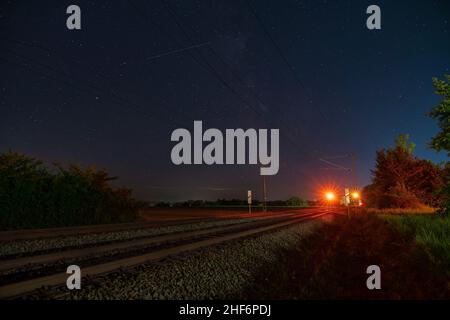 Milkyway mit seinem galaktischen Zentrum über einer einsamen Eisenbahnstrecke, die in einer sternenklaren Nacht über dem Stoppsignal steht Stockfoto