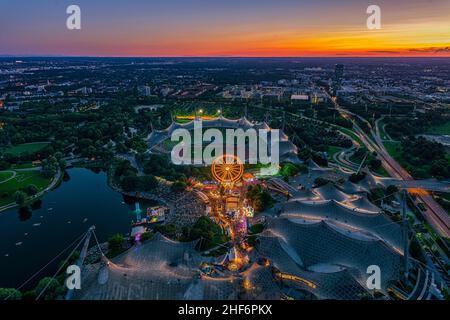 Wunderbarer Münchner Sonnenuntergang aus der Höhe mit einem Festival im beliebten Olympiapark und dem Stadion bei leuchtender orangefarbener Dämmerung Stockfoto