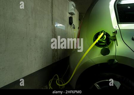 Ein eingestecktes elektrisches Kabel vom Typ 2 an der Ladebuchse eines Elektroautos mit der Wallbox, der heimischen Ladestation im Hintergrund. Konzept für den trending Lebensstil der Betankung Ihres Autos Stockfoto