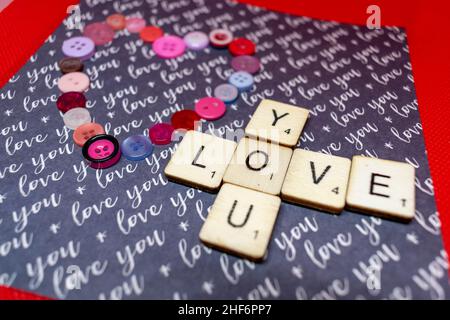 Liebe und Romantik Konzept. Love Heart Form aus rosa und roten Knöpfen mit scrabble spielen Würfel Rechtschreibung Love You. Romantischer Valentinstag Stockfoto