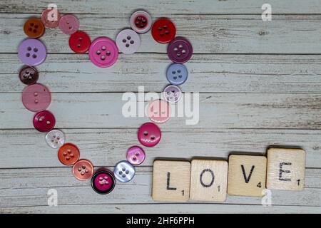 Liebe und Romantik Konzept. Love Heart Form aus rosa und roten Knöpfen mit scrabble spielen Würfel Rechtschreibung Love You. Romantischer Valentinstag Stockfoto