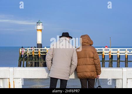 Ältere Ehepaare in warmen Mänteln auf dem hölzernen Pier an der Hafeneinfahrt Nieuwpoort / Nieuport entlang der belgischen Nordseeküste im Winter, Wes Stockfoto