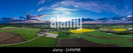 Landwirtschaftlicher Blick über wachsende Felder und ein idyllisch platziertes Dorf im Hintergrund, eingefangen von einer Drohne mit Kopierplatz in südbayern, deutschland Stockfoto