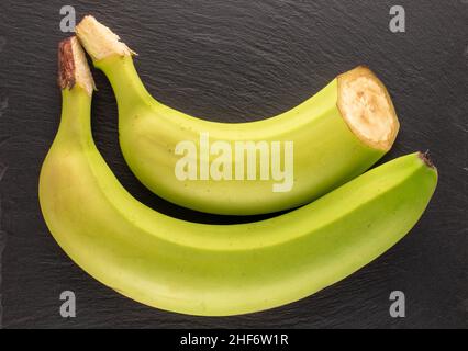 Eine ganze und halb organische grüne Bananen auf einem Schieferstein, Makro, Draufsicht. Stockfoto