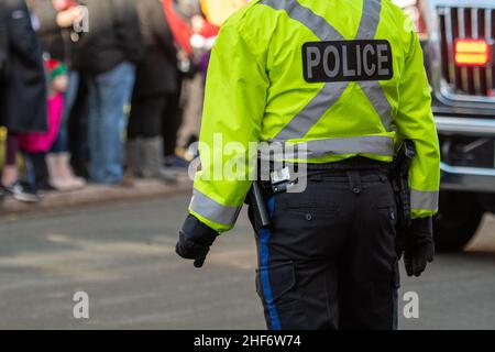 Polizeibeamter, in fluoreszierender Kleidung, in einer überfüllten Straße stehend. Der Beamte trägt eine kugelsichere Weste mit dem Wort Polizei auf ihrem Rücken Stockfoto