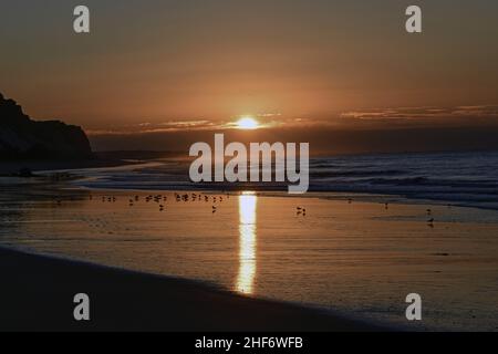 Sonnenaufgang am Strand von Albufeira, Surfen im Atlantik im Hintergrund Stockfoto