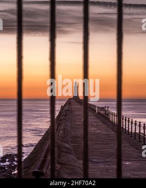 Tynemouth Pier und der Leuchtturm durch die Metallgeländer mit einem wunderschönen, lebhaften Sonnenaufgang Stockfoto