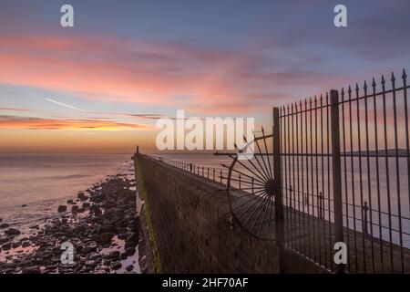 Tynemouth Pier und der Leuchtturm durch die Metallgeländer mit einem wunderschönen, lebhaften Sonnenaufgang Stockfoto