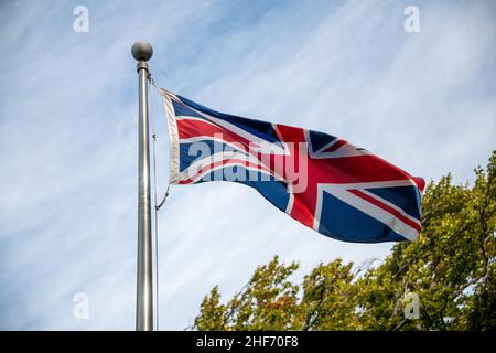 Die europäische Flagge wird als Union Jack bezeichnet, der auf einem Metallmast mit blauem Himmel und Wolken im Hintergrund fliegt. Es ist eine rote, weiße und blaue Flagge. Stockfoto