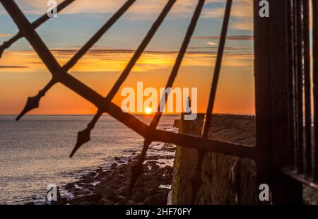 Tynemouth Pier und der Leuchtturm durch die Metallgeländer mit einem wunderschönen, lebhaften Sonnenaufgang Stockfoto