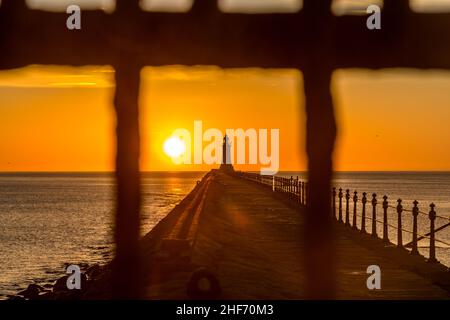 Tynemouth Pier und der Leuchtturm durch die Metallgeländer mit einem wunderschönen, lebhaften Sonnenaufgang Stockfoto