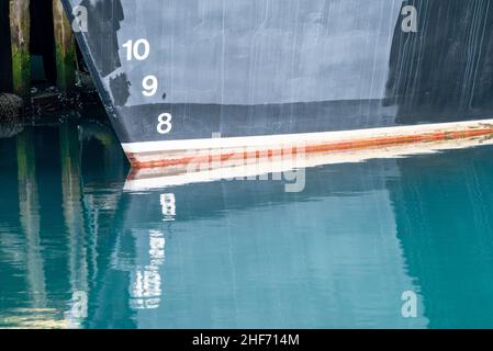 Ein marineblaues Schiff mit weißen und roten Wasserlinien-Markierungen. Die Zahlen sind auf der Unterseite der Bootsnummern gemalt, die sich in Wasser spiegeln. Stockfoto