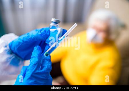 Doktor, der einer älteren Frau in ihrem Haus im Wohnzimmer eine Injektion gab Stockfoto