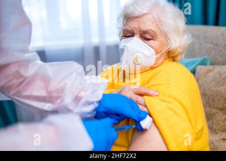 Doktor, der einer älteren Frau in ihrem Haus im Wohnzimmer eine Injektion gab Stockfoto