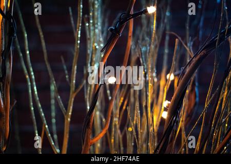 Bokeh verschwommenes Foto von funkelnden leuchtenden Lichterketten mit braunen Zweigen und goldenem Glitzer auf einem verschwommenen orangefarbenen und braunen Backsteinwand-Hintergrund. Chris Stockfoto