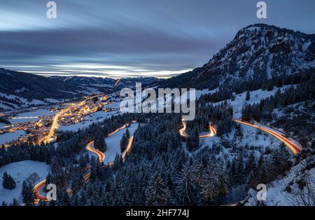 Bad Hindelang und Jochpassstraße erleuchtet am Abend in einer verschneiten Winterlandschaft. Umrahmt von den schneebedeckten Allgäuer Alpen. Bayern, Deutschland, Europa Stockfoto