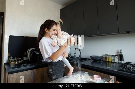 Glücklich fürsorgliche Mutter kocht Essen in der Küche mit einem kleinen Kind in den Armen Stockfoto